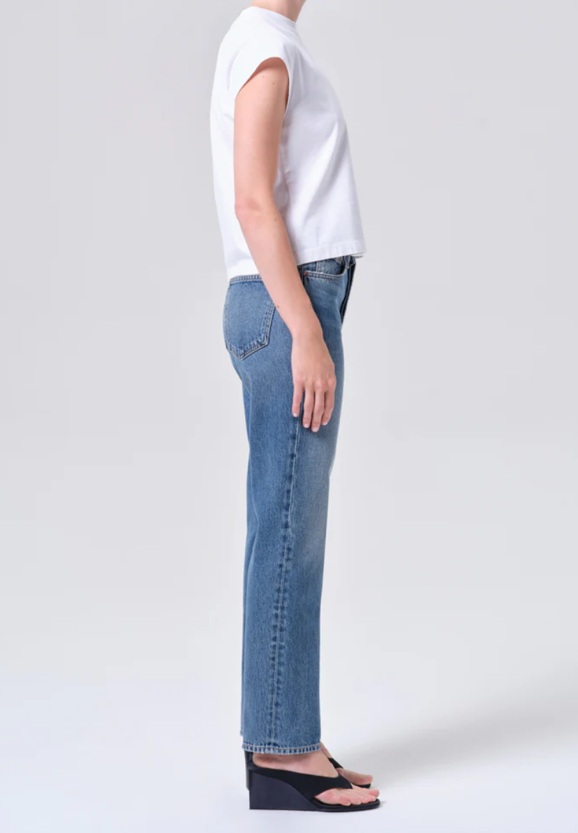 A person in profile wears a white short-sleeve top, AGOLDE Lana Jean - Liberty high-waisted straight jeans made from regenerative cotton denim, and black wedge sandals, set against a plain light background.