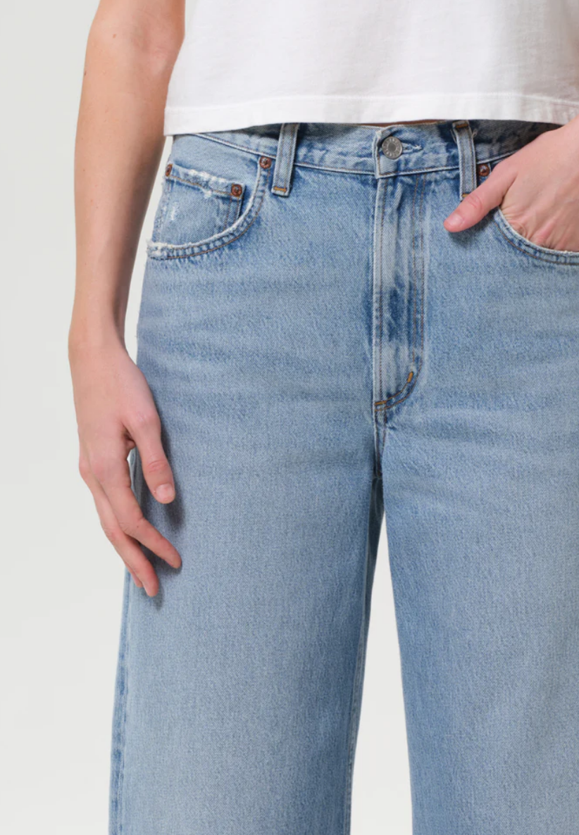 A person wearing AGOLDE’s Low Curve Fray - Force jeans, featuring a frayed hem and relaxed fit, crafted from regenerative cotton.