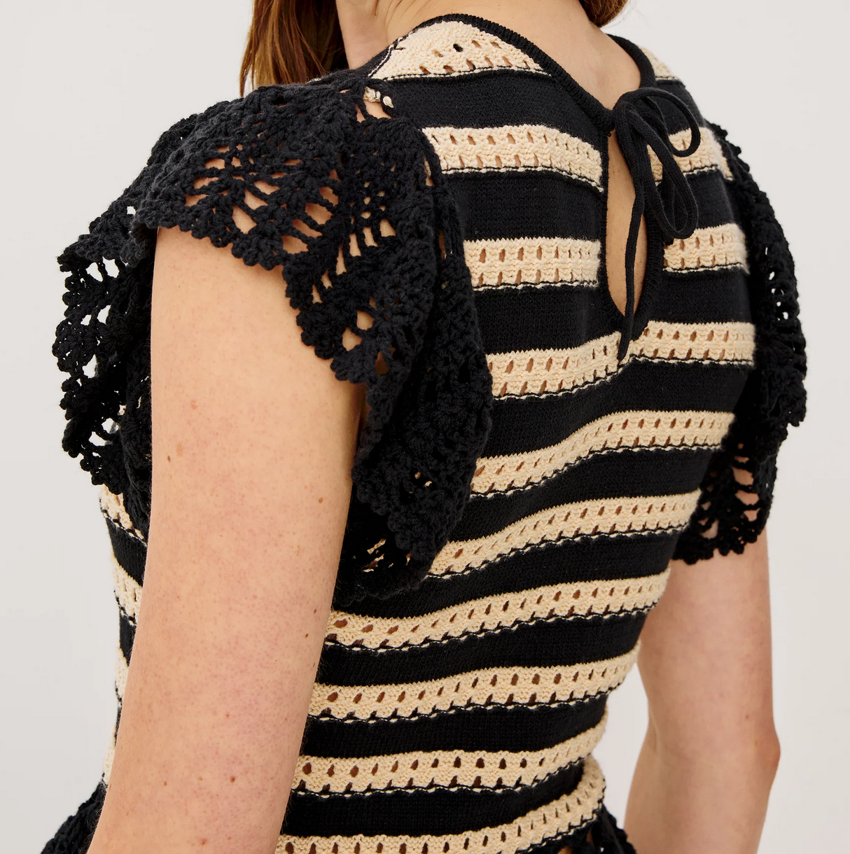 A close-up of a woman wearing the Rails Coen Knit Top in black stripe, featuring short sleeves, lace accents, a peplum hem, and a back neck tie—showcasing chic nautical-inspired style.