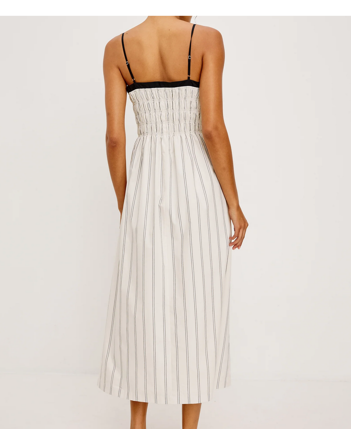 A woman is seen from the back wearing the Rails Primrose Dress in Ecru Stripe—a sleeveless midi dress with thin shoulder straps and black and white vertical stripes.