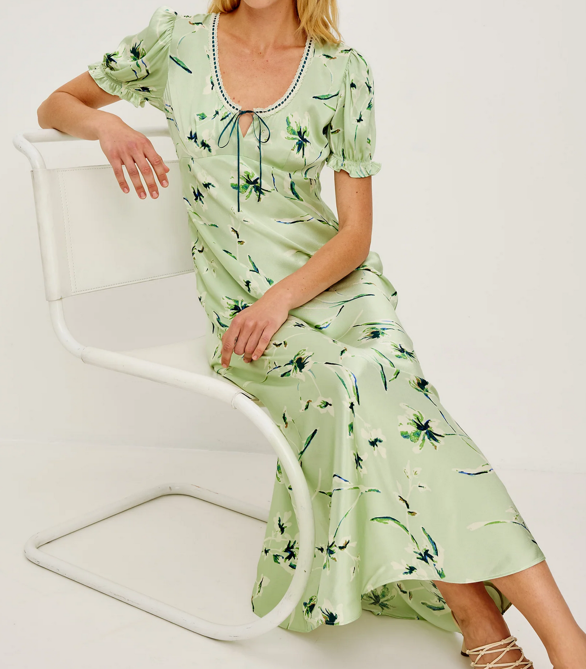 A person wears the Rails Allison Dress in mint—a light green, floral satin crepe maxi—while seated on a white modern chair against a plain background.