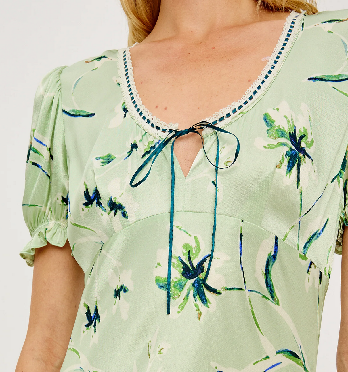 Close-up of the Rails “Allison Dress” in mint, featuring light green satin crepe with a floral pattern, puffed short sleeves inspired by a blouse, and a keyhole neckline tied with a thin ribbon.