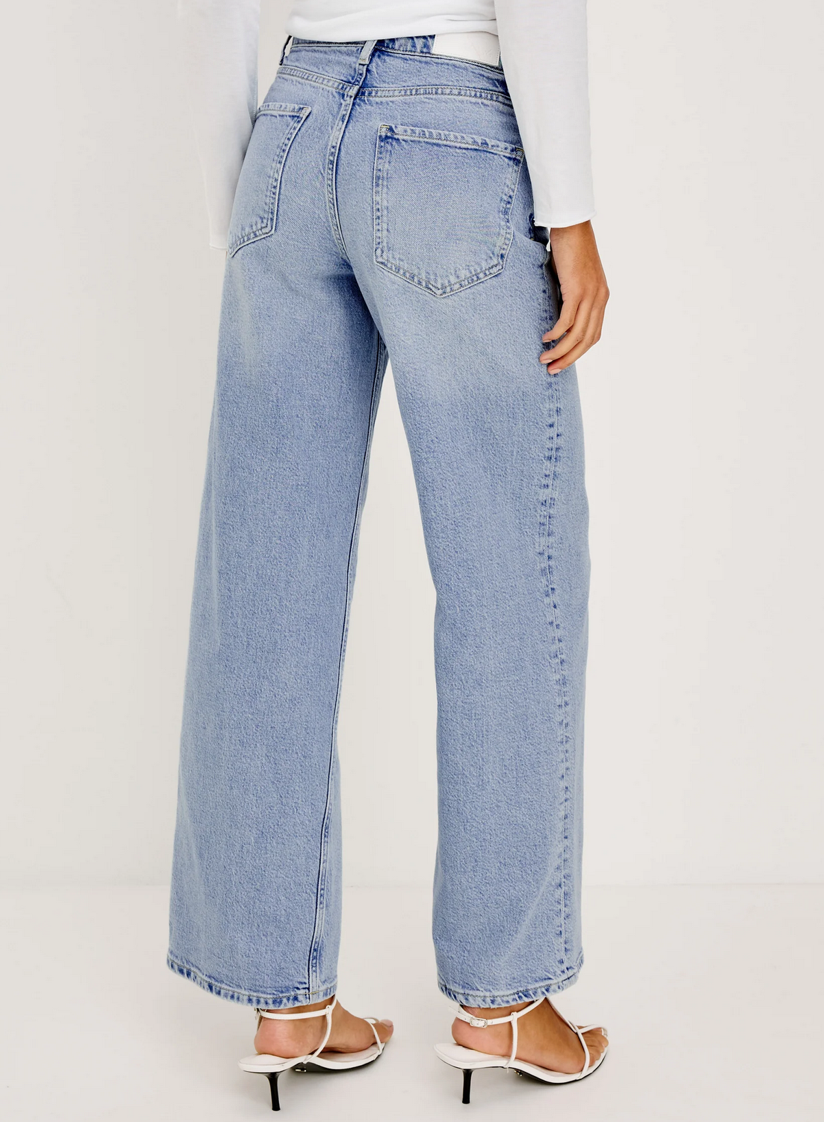 A person wearing Rails Getty Wide Leg jeans in light blue with white heeled sandals, shown from the back, highlights an effortless hourglass silhouette.