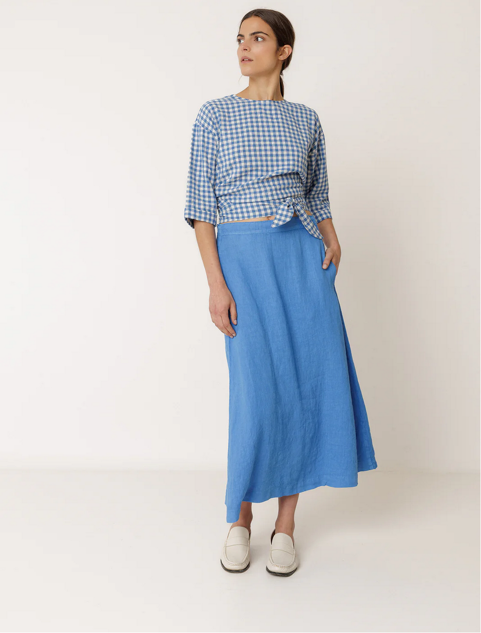 woman wears long linen blue skirt with a matching top byy indi and cold on a white background.