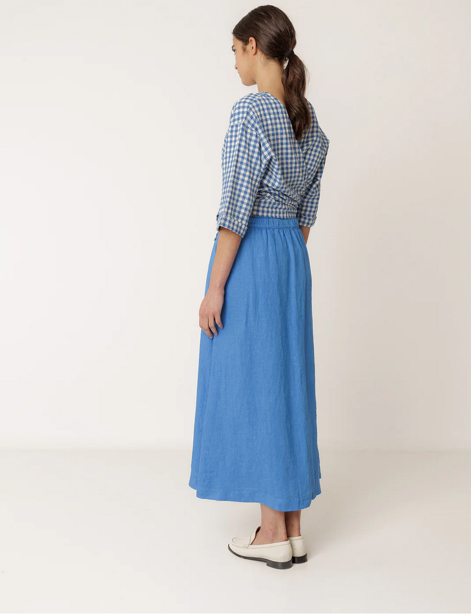 woman wears long linen blue skirt with a matching top byy indi and cold on a white background.