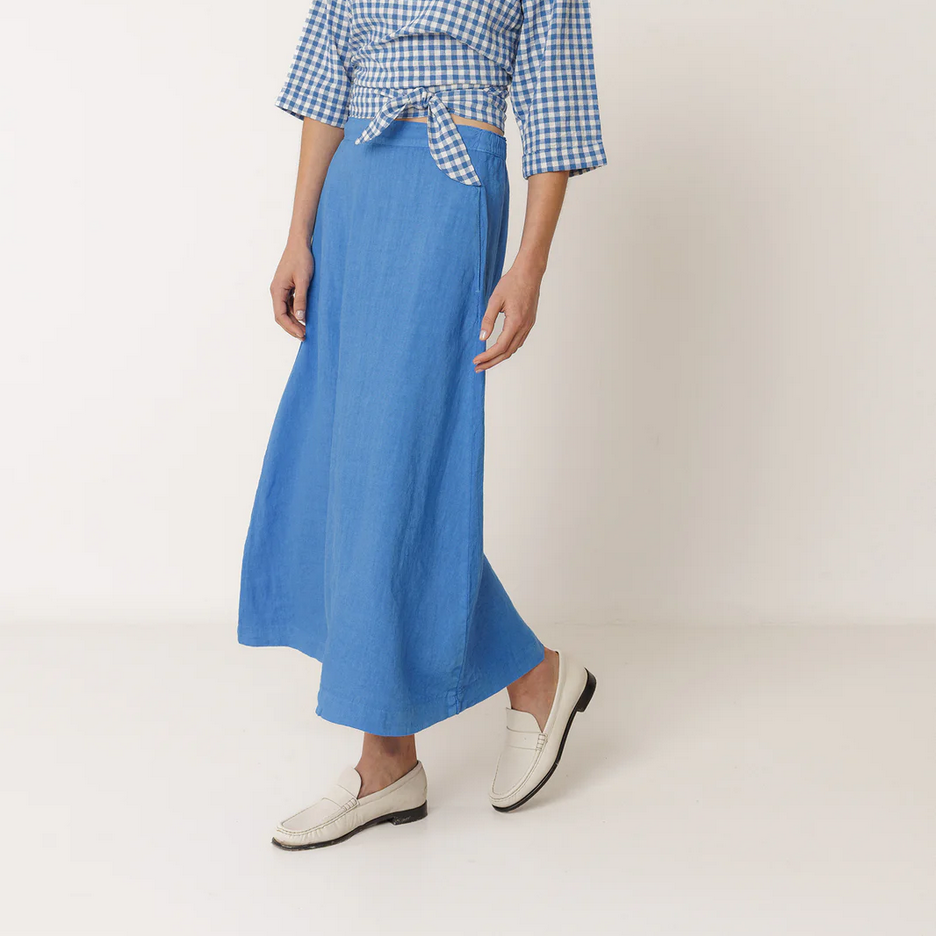woman wears long blue linen skirt with a wrap top both by indi and cold