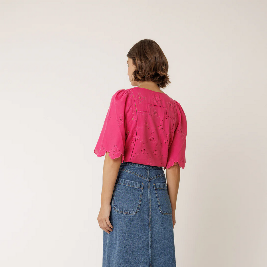 Person wearing a pink top by indi and cold and blue denim skirt on a white background