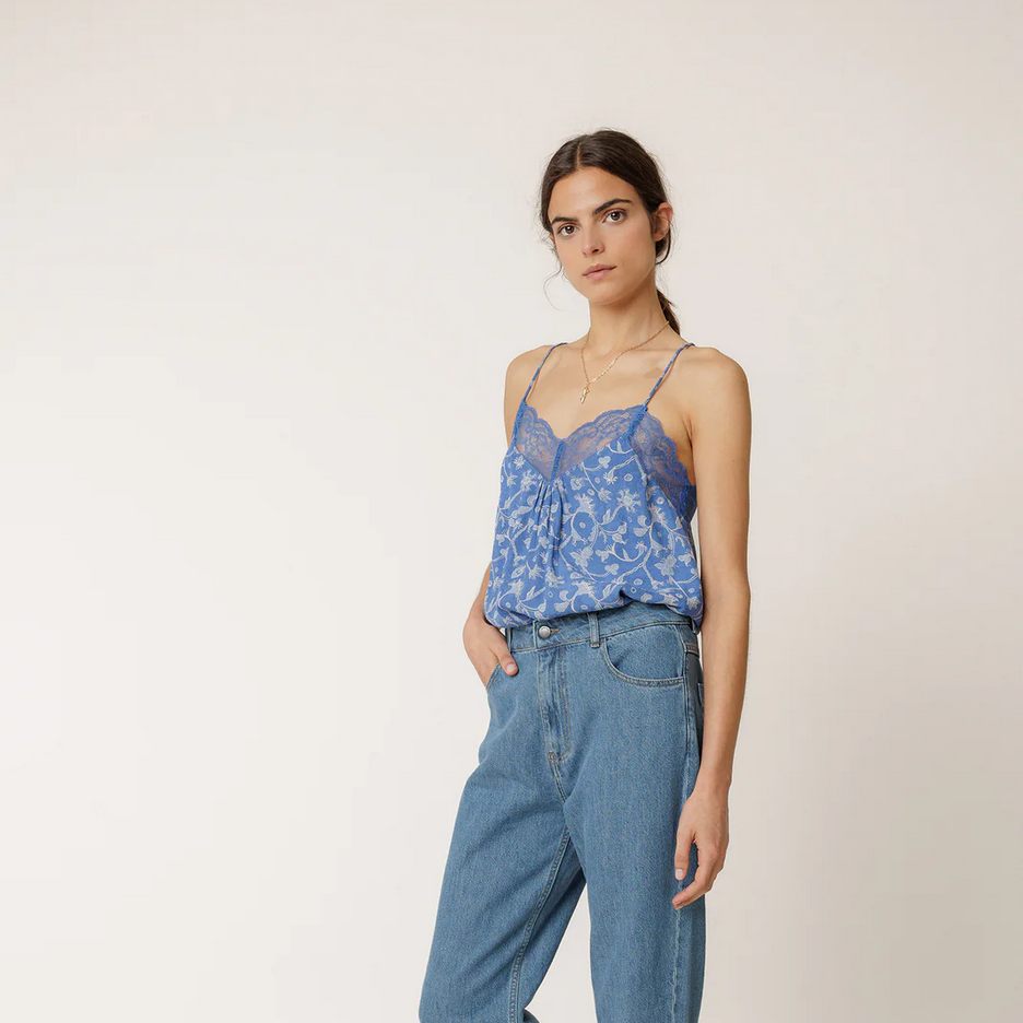 Woman wearing an indi and cold sustainable blue floral top and jeans on a white background