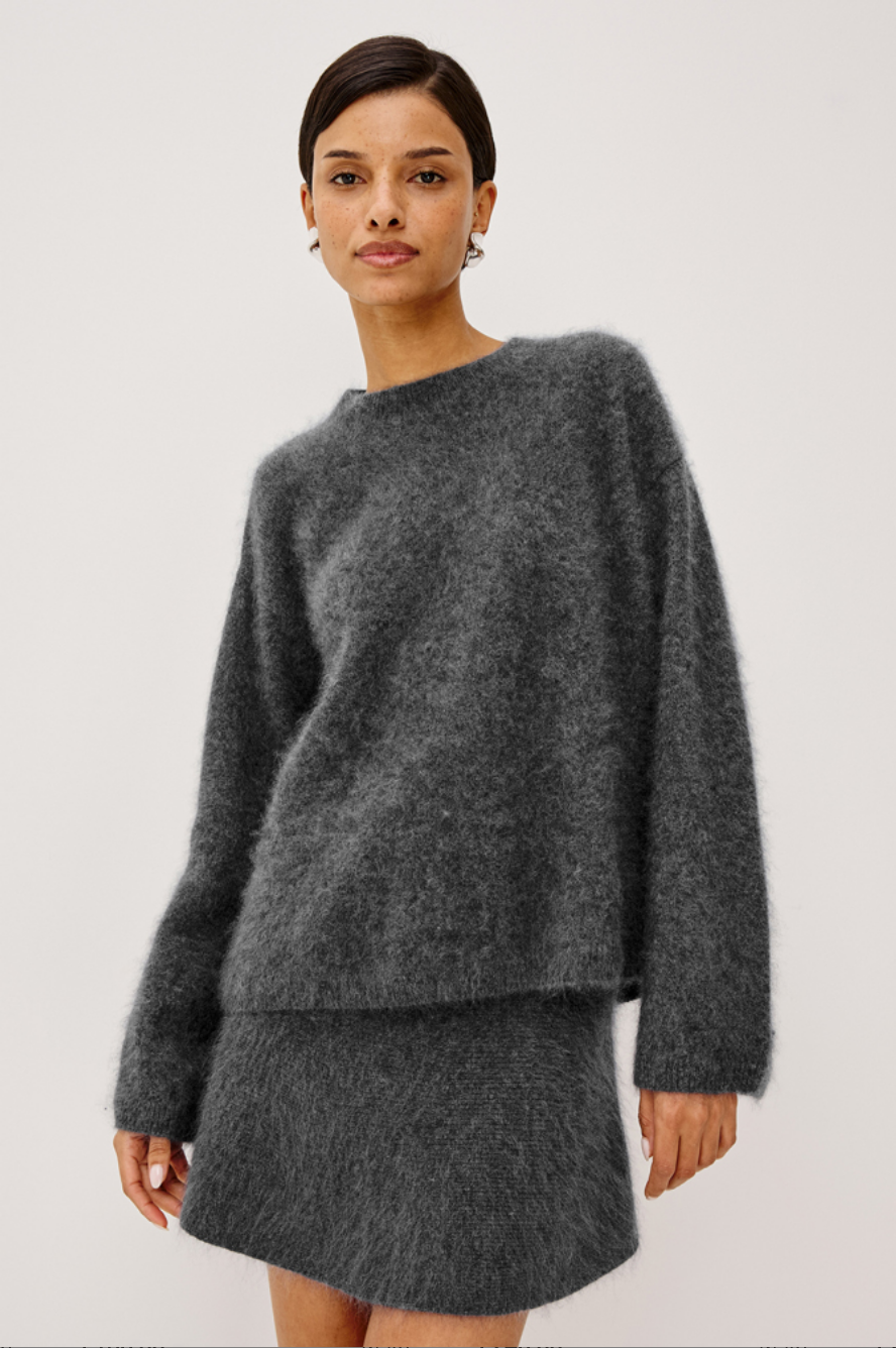 A model wearing a dark gray brushed wool knit sweater and matching mini skirt against a plain light gray studio background.