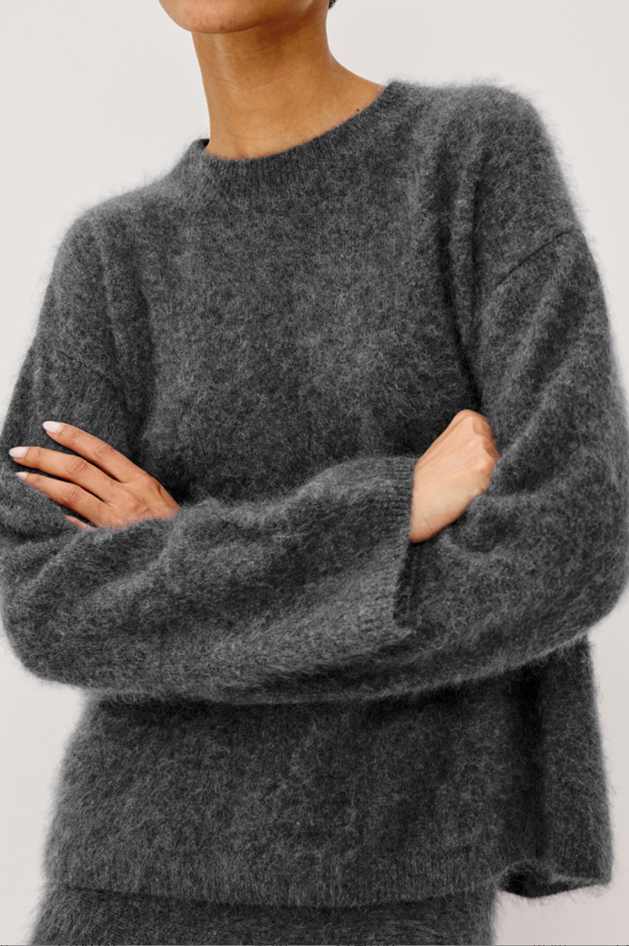 A model wearing a dark gray brushed wool knit sweater and matching mini skirt against a plain light gray studio background.