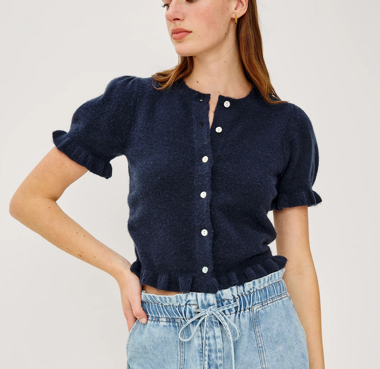 Woman wearing a navy blue knitted cardigan with white buttons on a plain background