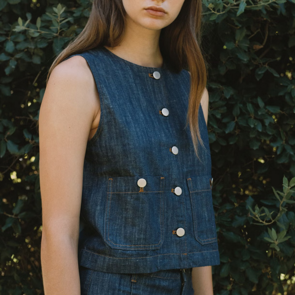 Woman wearing a tiny big sister denim sleeveless top and pants against a natural background
