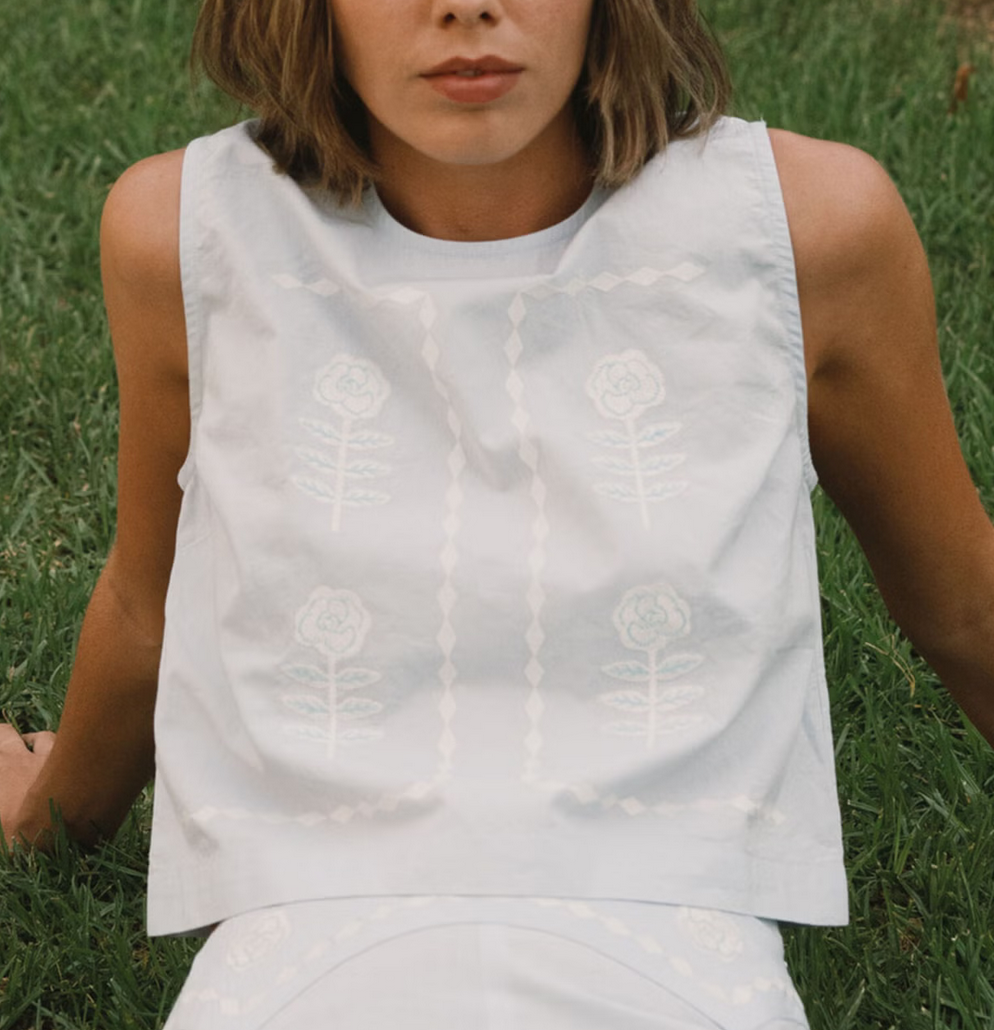 Person wearing a white sleeveless top and pants sitting on grass.