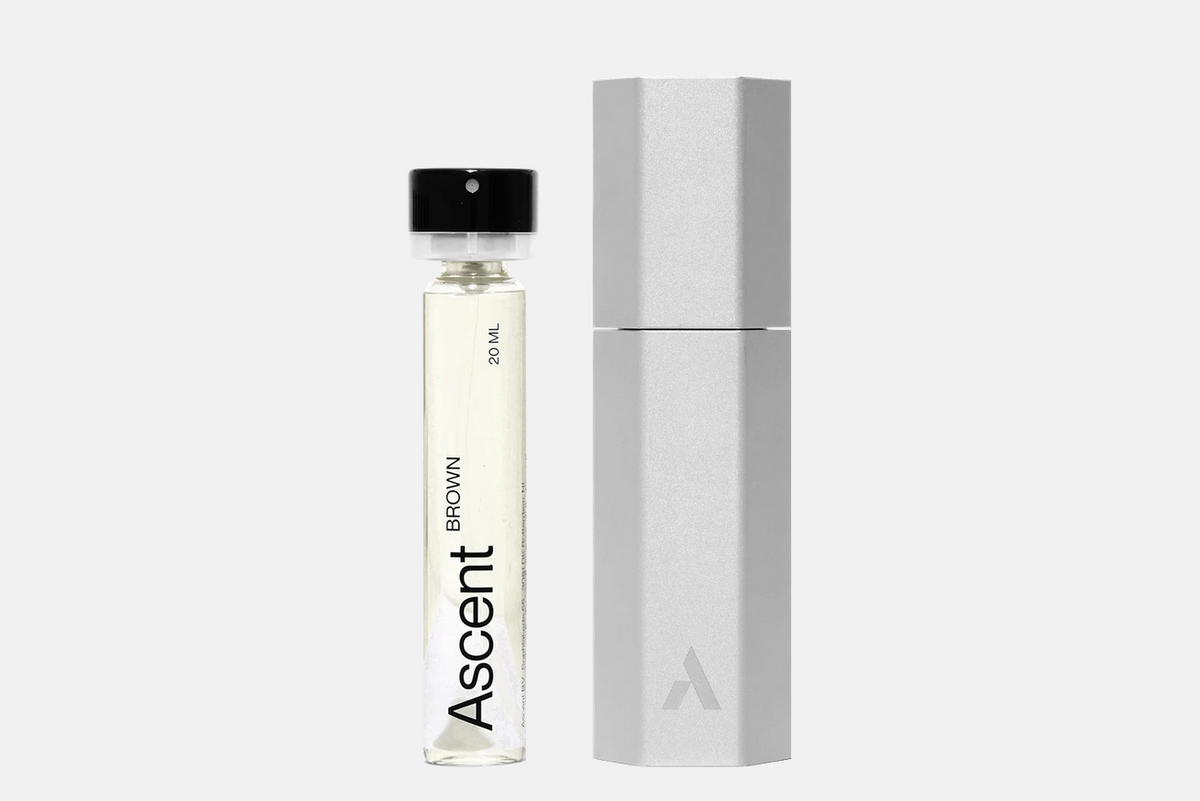 An Ascent Starter Pack - Brown 20 ml sandalwood perfume vial with a black cap, standing next to its hexagonal silver cylindrical case.
