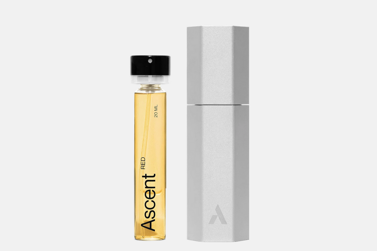 A glass vial of Ascent Starter Pack - Red perfume extract filled with amber liquid next to a hexagonal silver case.
