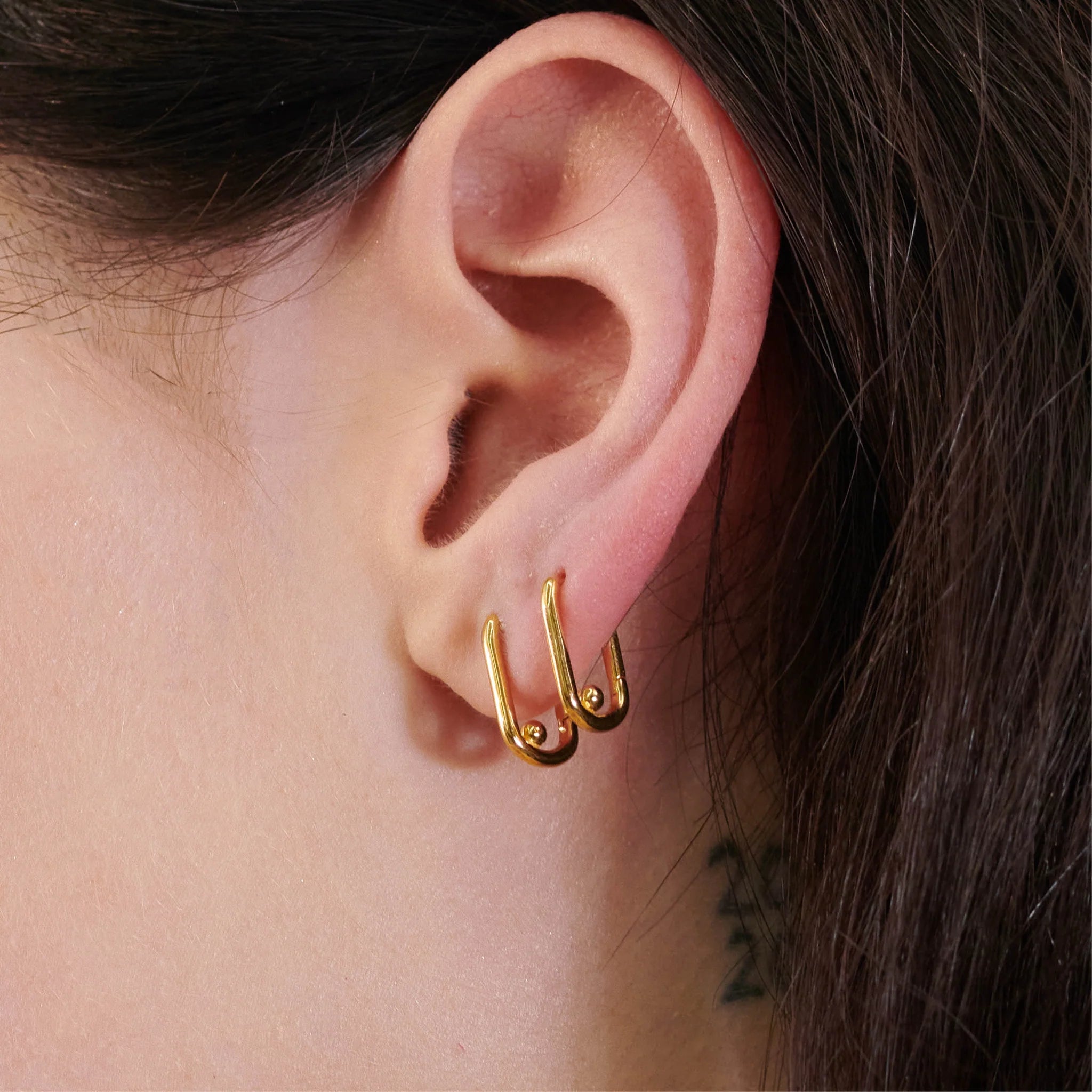 A woman's ear with a Stellar Hardware Huggie Hoop Earring in Gold by Rachel Jackson featuring a click mechanism for easy wear.