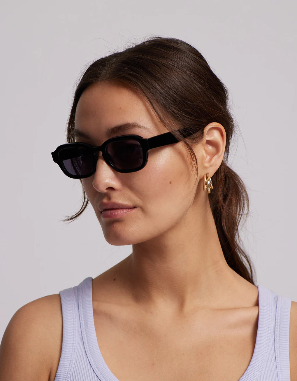 The Colorful Standard Sunglass 01 - Deep Black model is sporting a chic black pair of sunglasses, providing UV400 protection for your eyes during any adventure. Completing the look, they are also wearing a stylish purple tank top.