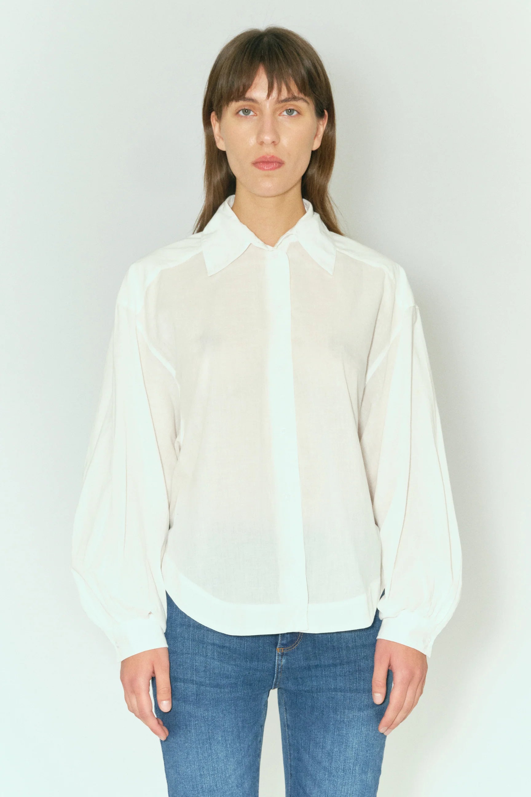 The model is wearing a Tomorrow Denim Sienna Supersized Shirt - Ecru, a white blouse made from organic cotton that is also machine washable.