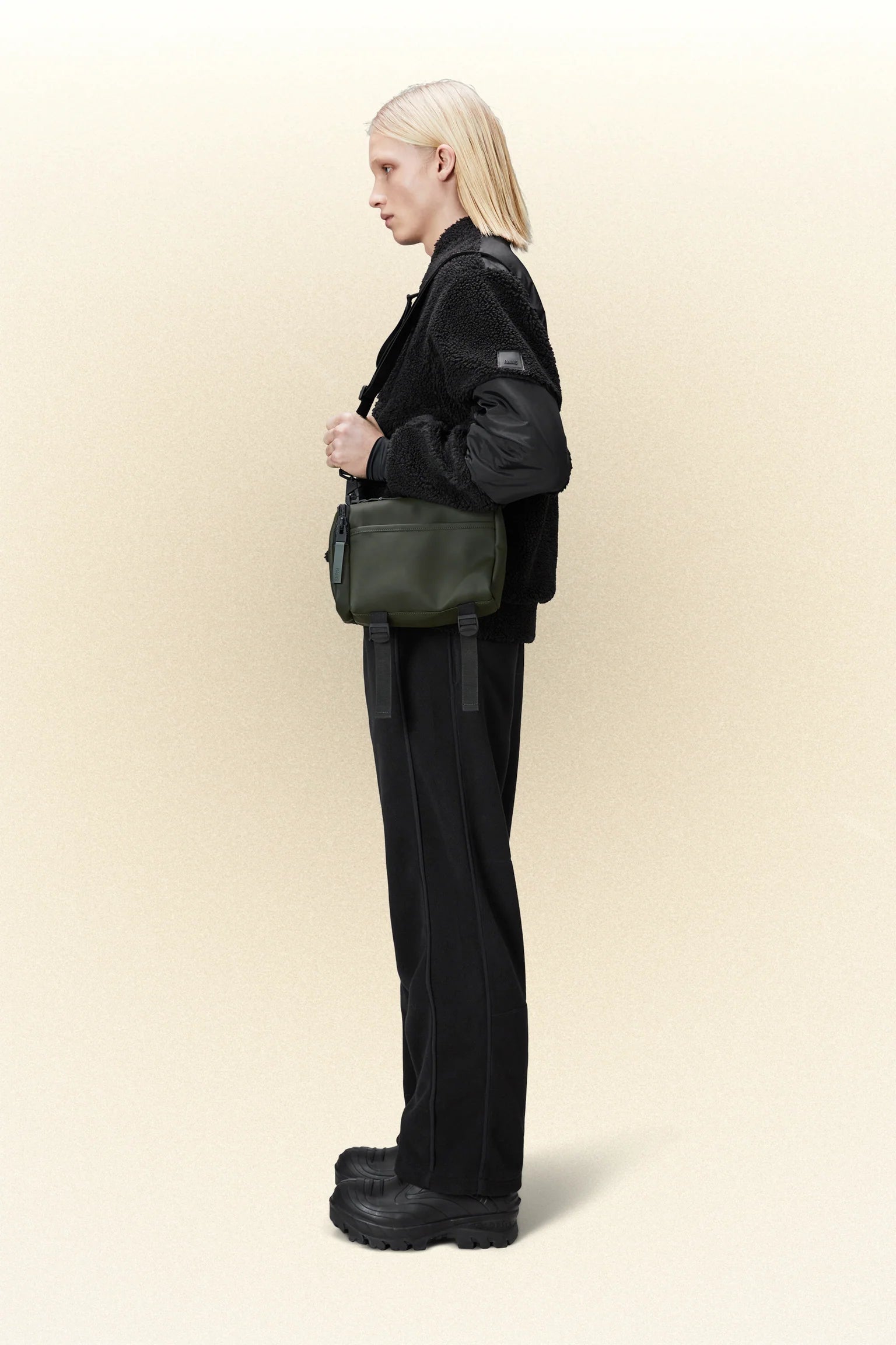 A woman wearing a black jacket and black pants with a waterproof black Rains texel crossbody bag in green, carrying her daily essentials.