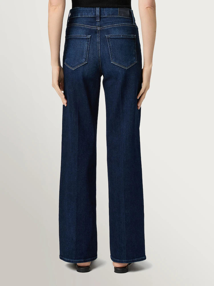 Person wearing Paige Anessa Wide Leg 31"- Duke of York jeans in dark blue stretch denim with black shoes, shown from the back against a plain light background.