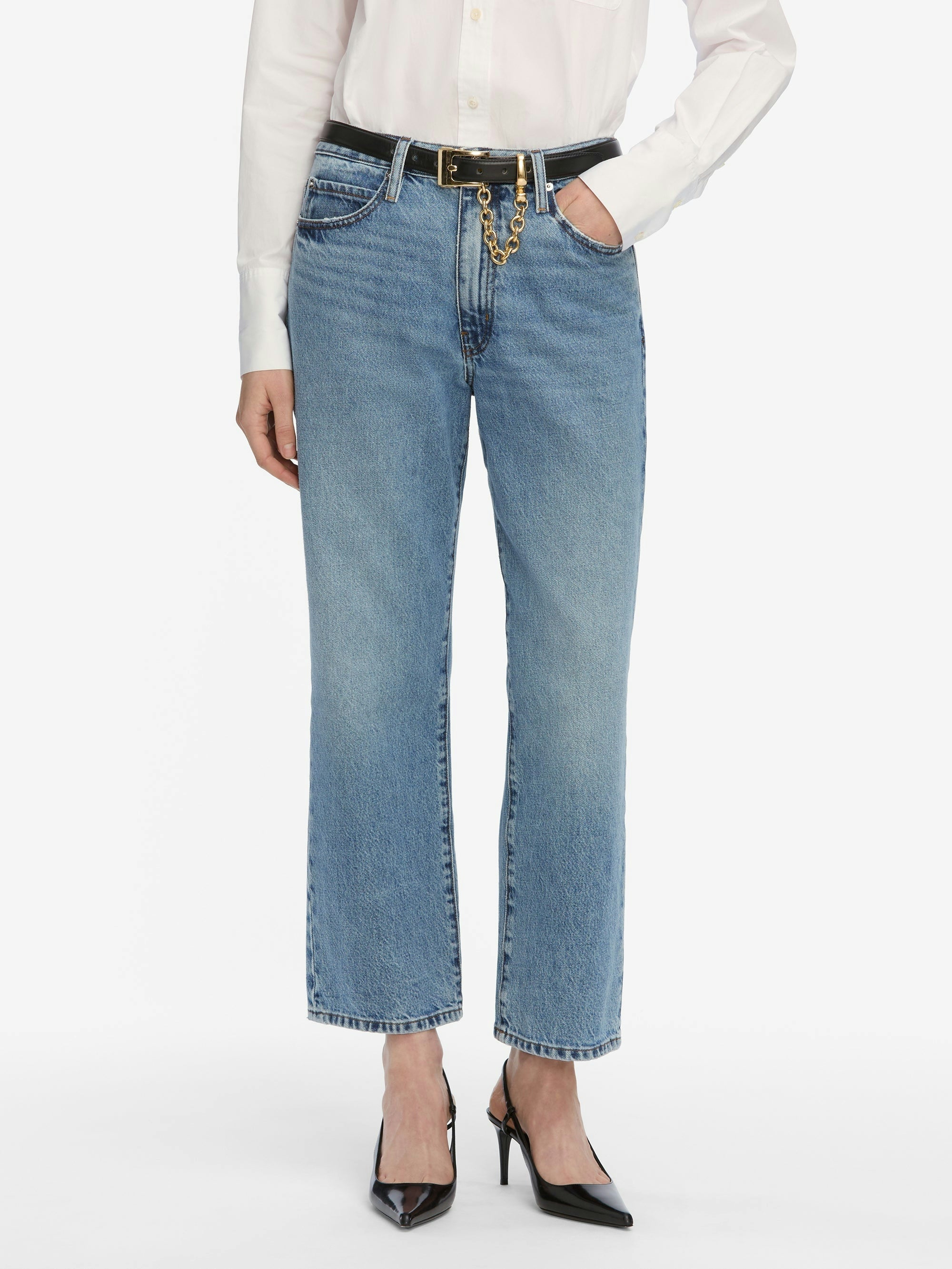Person wearing light blue jeans with a white top and black shoes on a white background