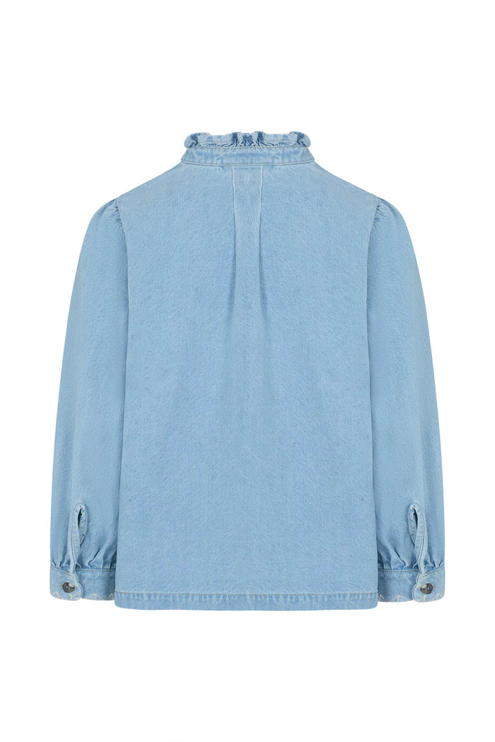 The Dana Denim Jacket - Sunbleached by Seventy & Mochi is shown from the back in light blue denim, featuring a ruffled collar, buttoned cuffs, and delicate geometric embroidery for a charming look.