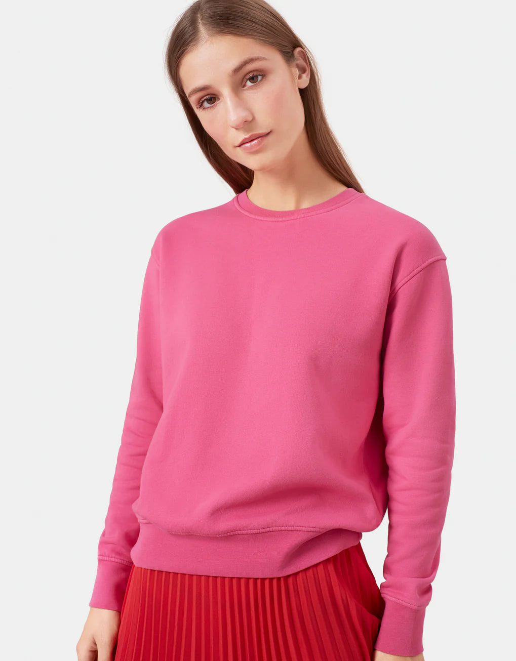 The model is wearing a pink Classic Organic Crew sweatshirt made by Colorful Standard.