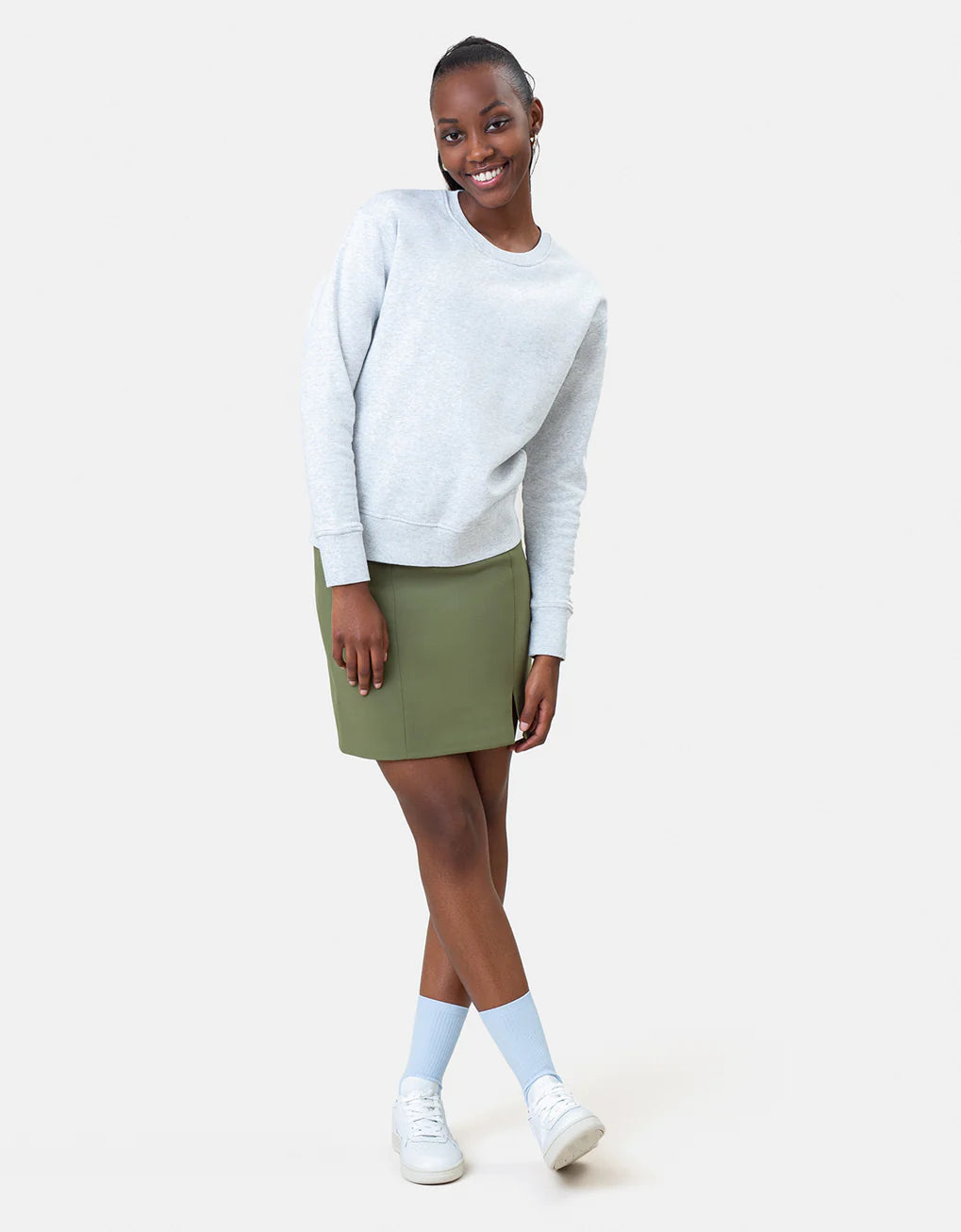 Woman in a Colorful Standard Classic Organic Crew sweater and green skirt posing with one hand on her hip, featuring an anti-pilling quality.