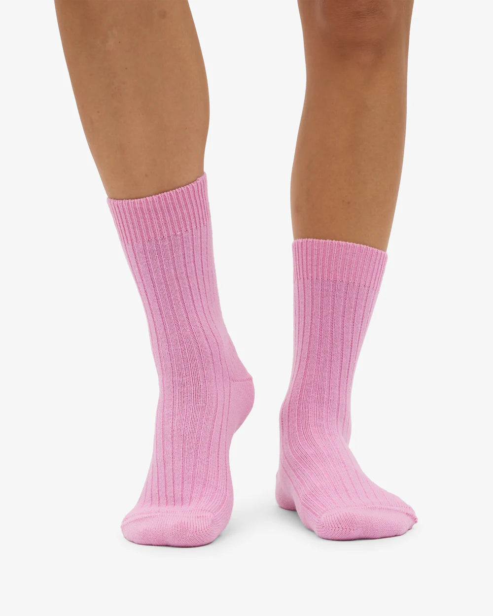 Someone stands on a white background wearing Colorful Standard Merino Wool Blend Socks in light pink, featuring ribbed knee-length design.