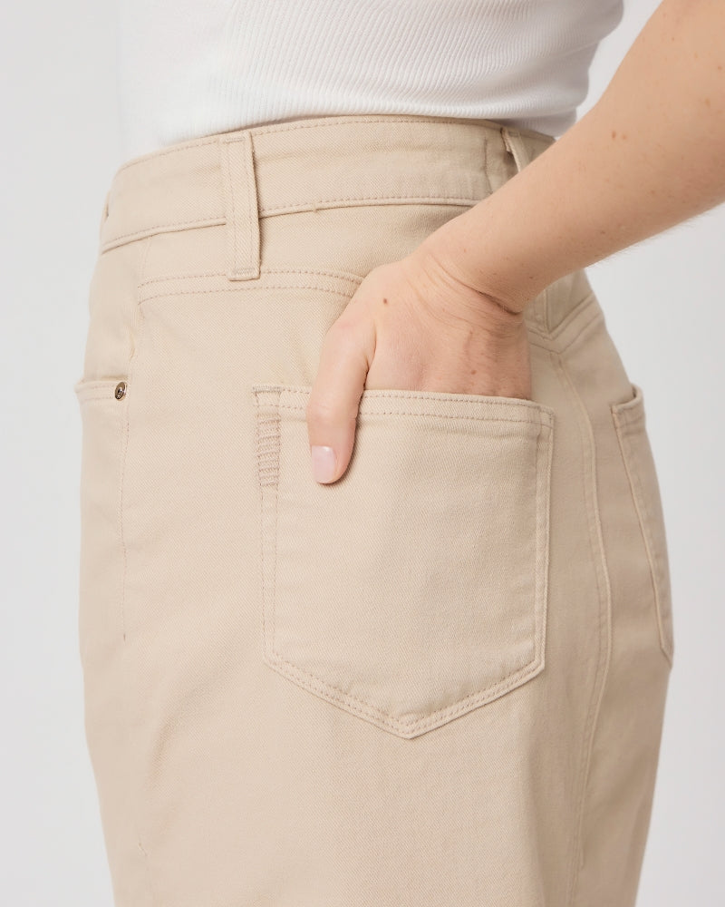 A person wearing high waist Angela Midi Skirt - Soft Beige pants with their right hand partially inserted into the back pocket.
