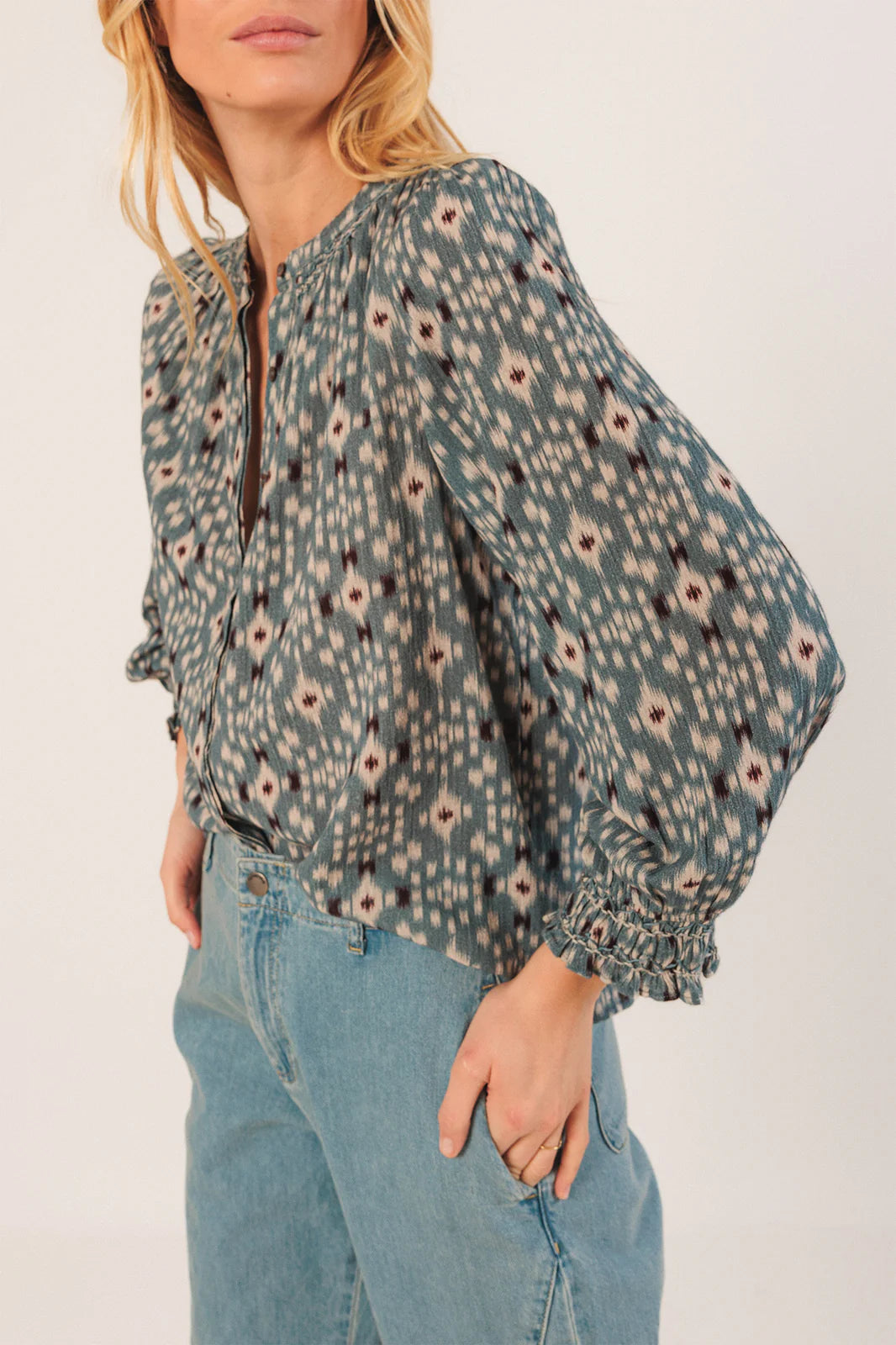 A woman wears the Indi & Cold Smock Detail Shirt in Vintage Blue with light blue high-waisted jeans, standing against a plain background.