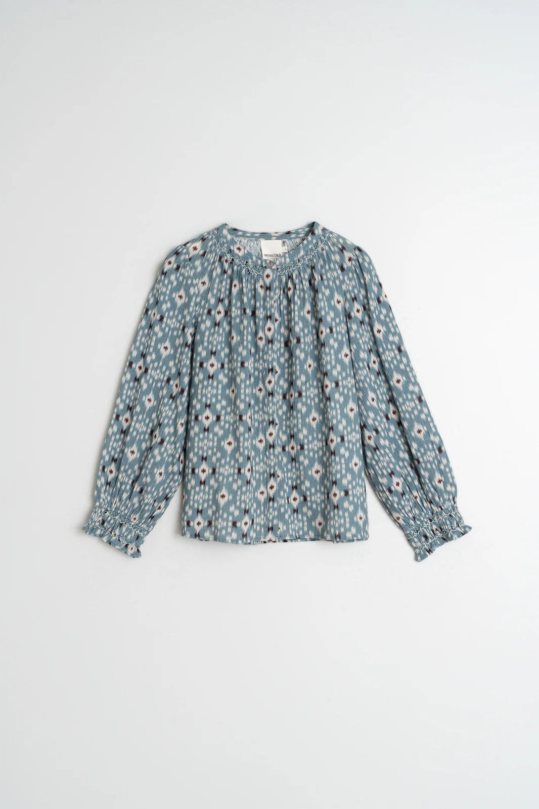 The Indi & Cold Smock Detail Shirt in Vintage Blue, featuring a white and black floral pattern, round neckline, and ruffled cuffs in soft organic cotton, is displayed flat on a white background.