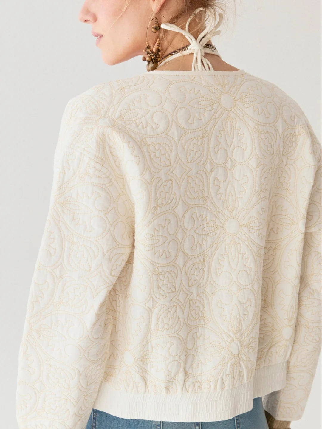 A woman exudes timeless elegance in the Maison Hotel Boticcelli Jacket - Tesela Ivory, featuring light embroidery with floral patterns. Seen from the side and back, she pairs it with earrings and an ivory cotton halter-style top tied at her neck.