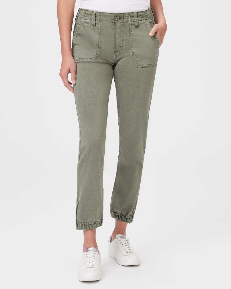 A woman dressed in army green hue pants, specifically the Paige Mayslie Jogger in Vintage Ivy Green, and a white t-shirt, perfectly capturing the utility trend.