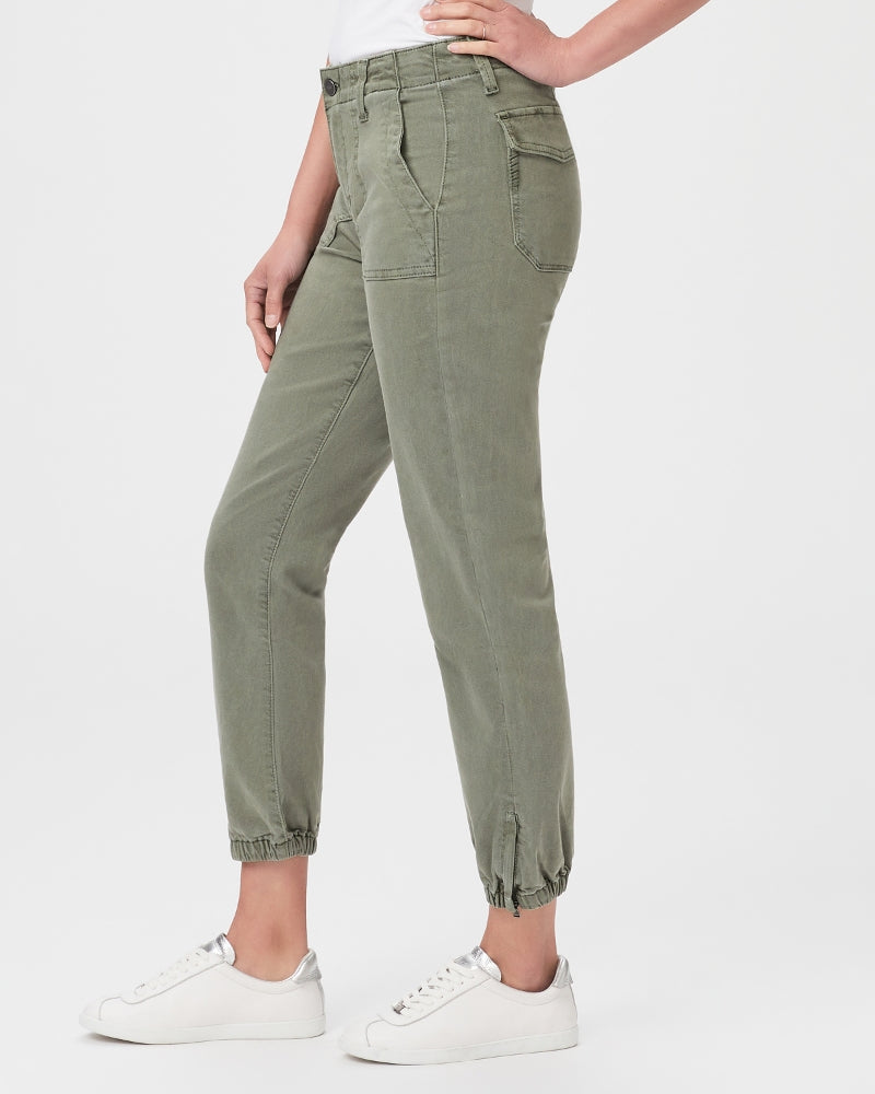 A woman donning the utility trend in Paige Mayslie Joggers, featuring a Vintage Ivy Green hue. She completes her outfit with white sneakers for a stylish and comfortable look.