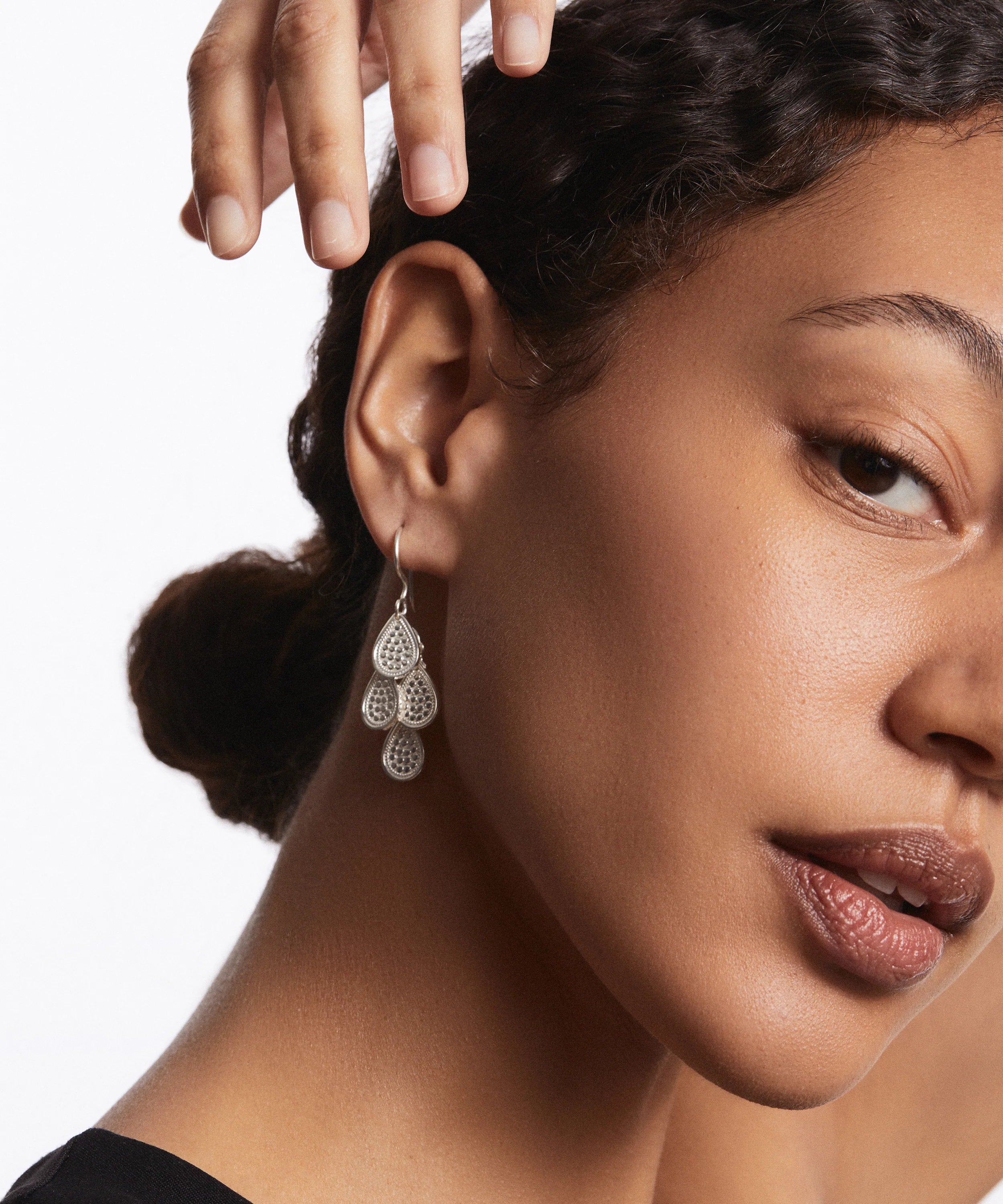 Close-up of a person showcasing the Classic Chandelier Earrings - Gold by Anna Beck, featuring a teardrop design and plated in 18k gold, while their hand rests above their head.