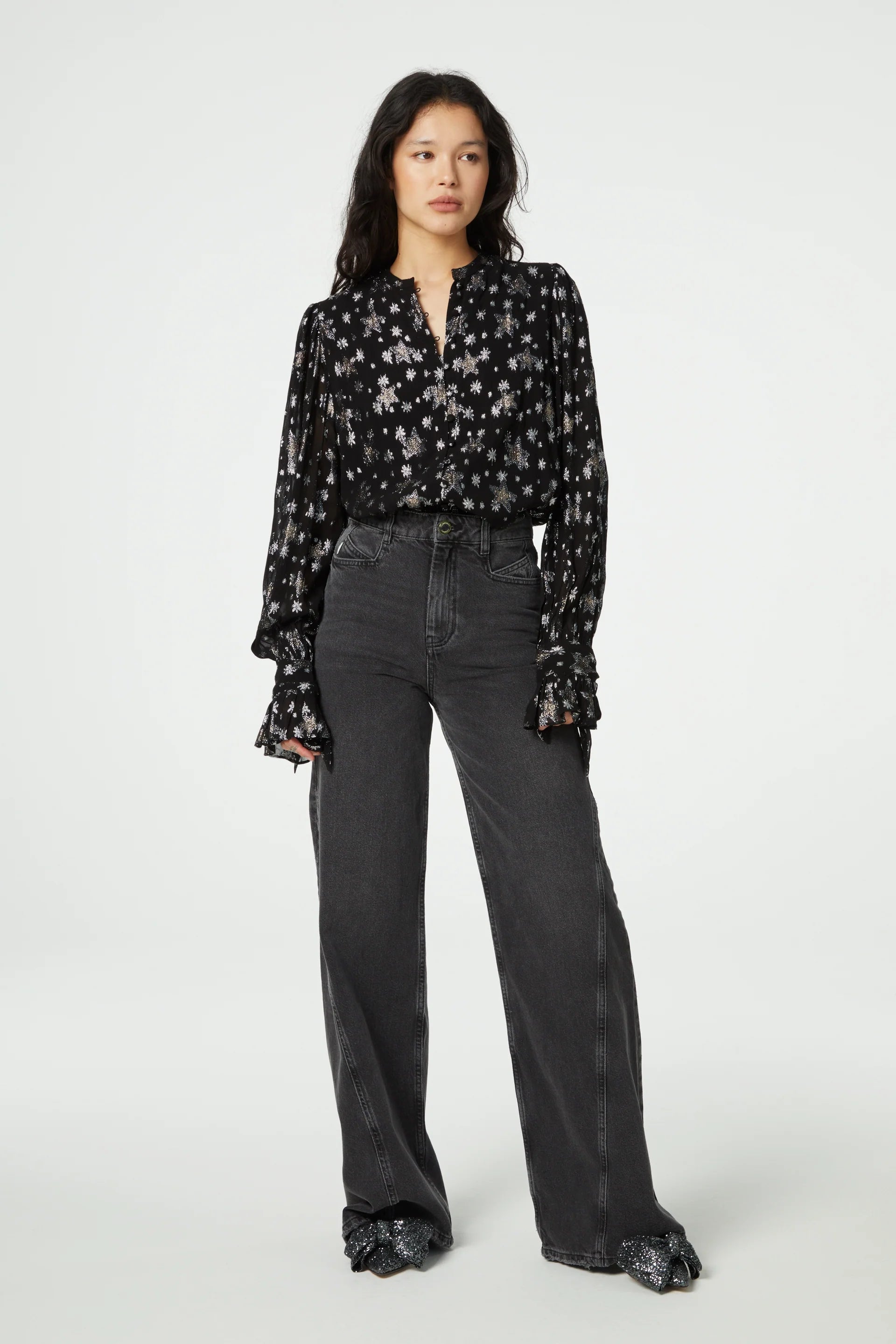 The model is wearing a Kylie Blouse - Starfleet by Fabienne Chapot, with long sleeves and a fabric-covered button closure, paired with wide leg jeans.