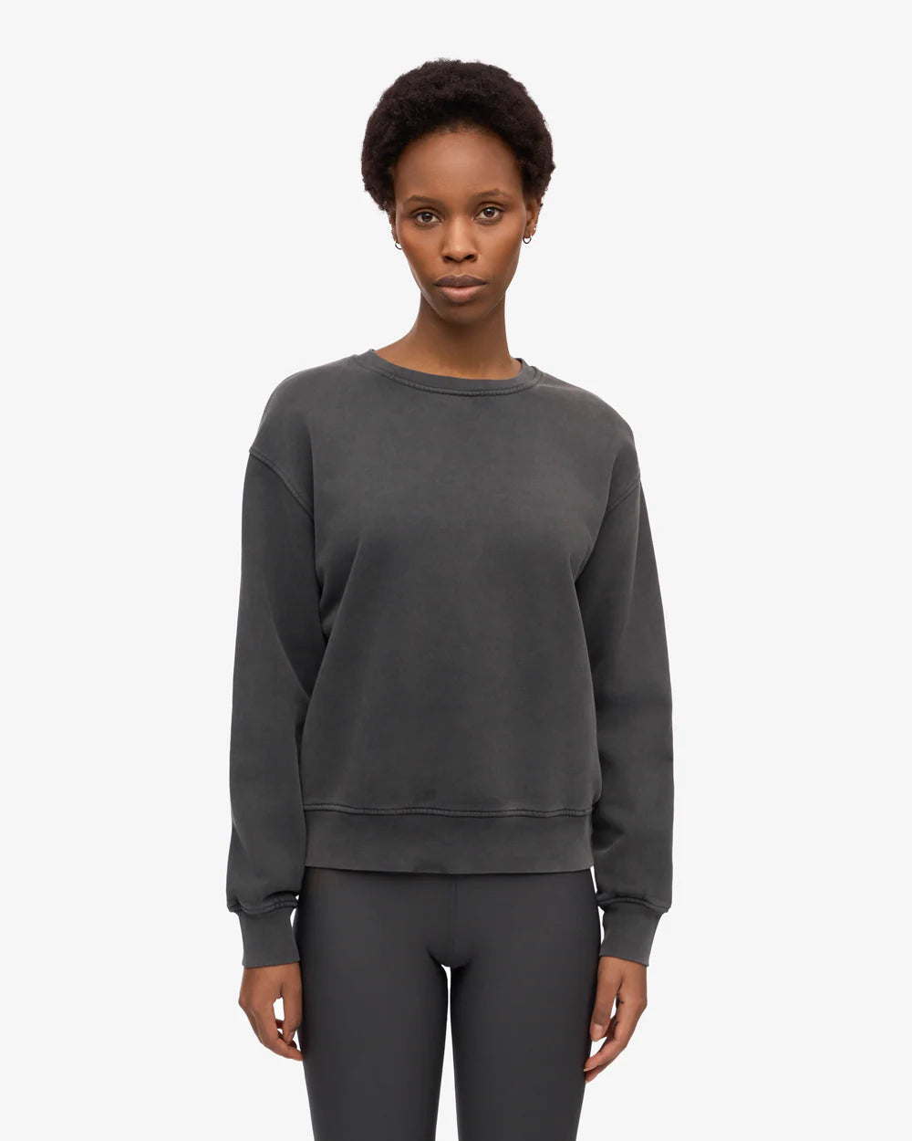 A person faces forward, wearing the Colorful Standard Classic Organic Crew in charcoal gray with matching leggings, against a plain white background.