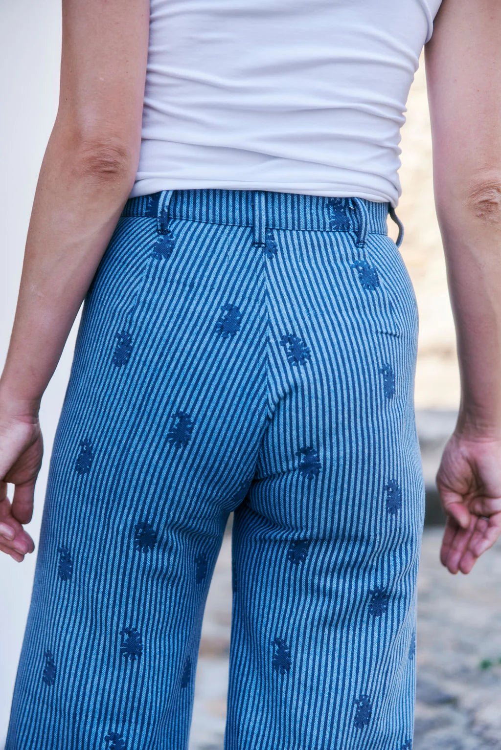 Wearing SZ Blockprints' Disco Pant - Denim Paisley, styled with a crisp white shirt, a person stands outdoors with hands relaxed at their sides.