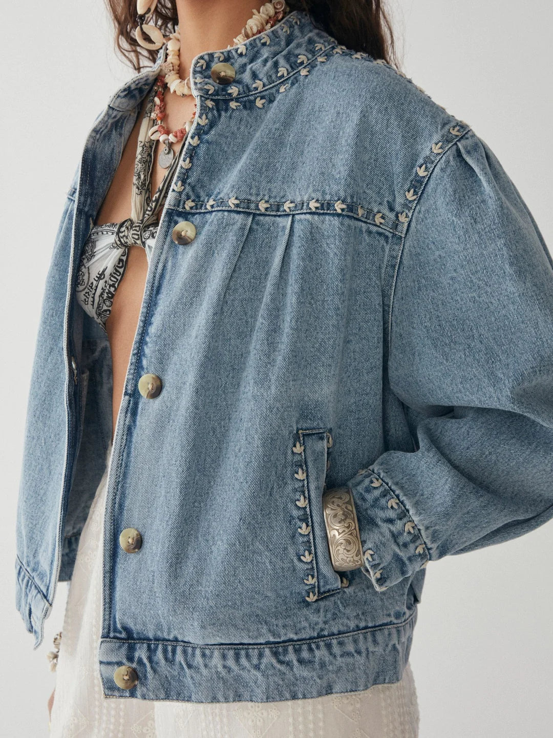 Model wears denim jacket with round collar and embroidered seams and cuffs