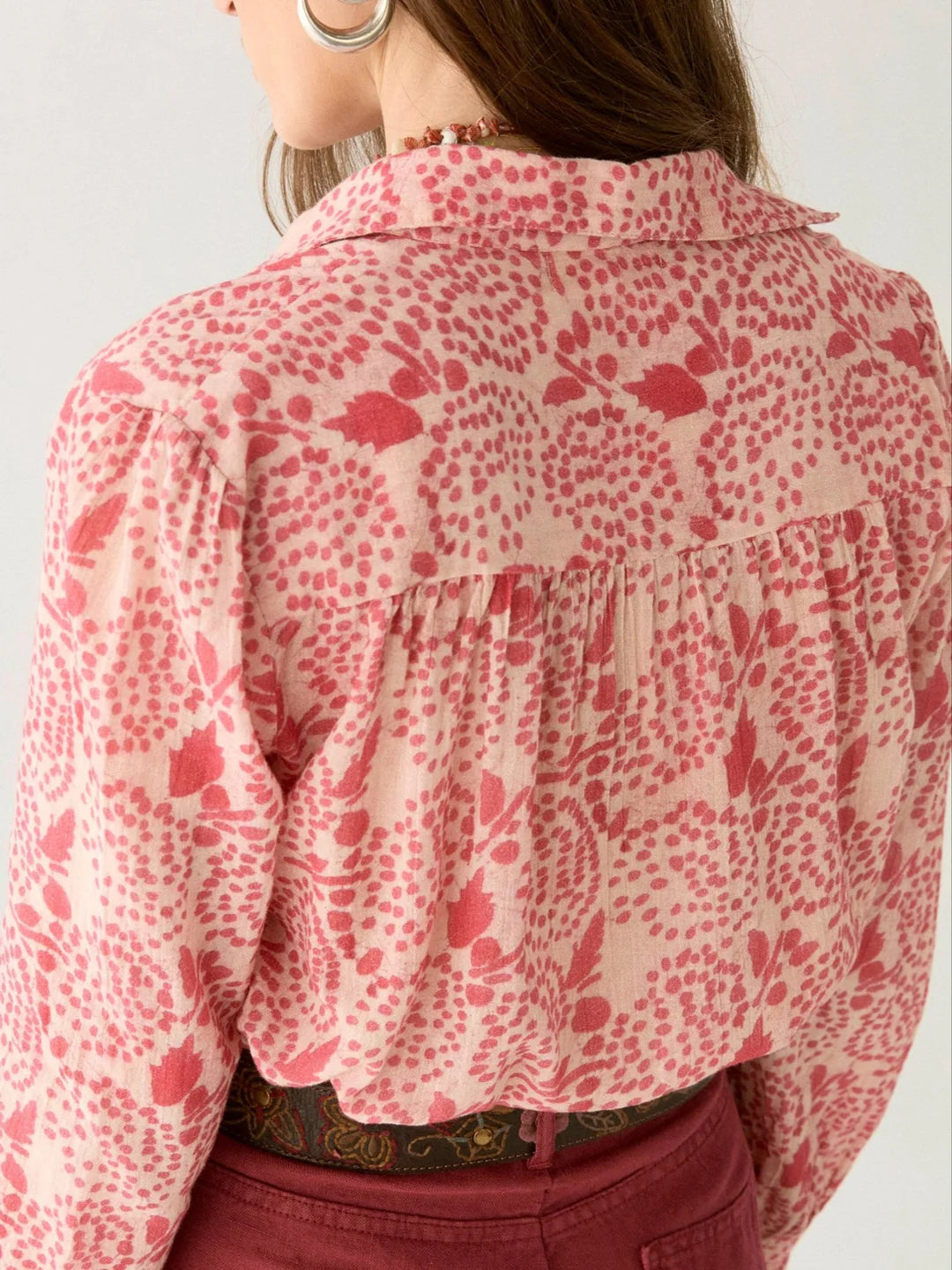 A person wearing a Maison Hotel's Dylan Blouse - Pink Martini in a pink and white floral pattern with gathered back details, paired elegantly with pink trousers.