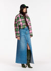 person wearing a black basball cap styles a cropped checked jacket in pink, green and black with a long maxi denim skirt,
