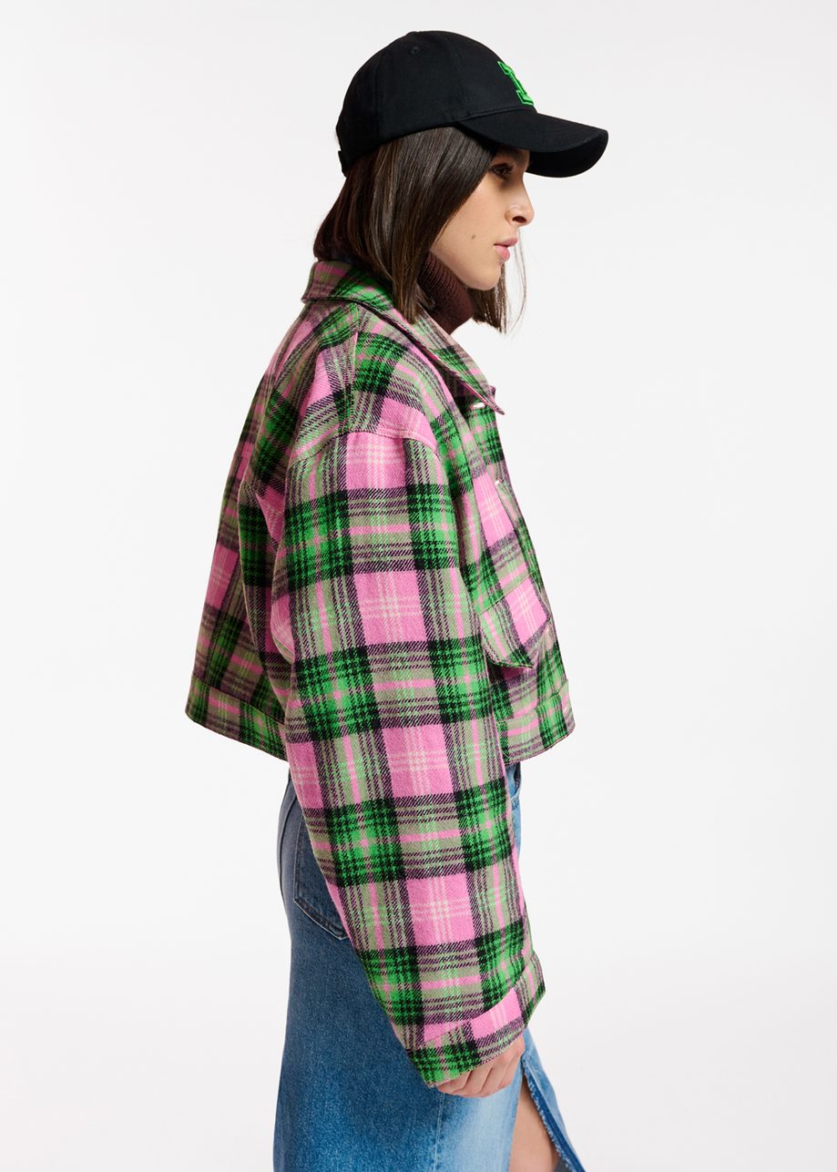 person wearing a black basball cap styles a cropped checked jacket in pink, green and black with a long maxi denim skirt, side view 