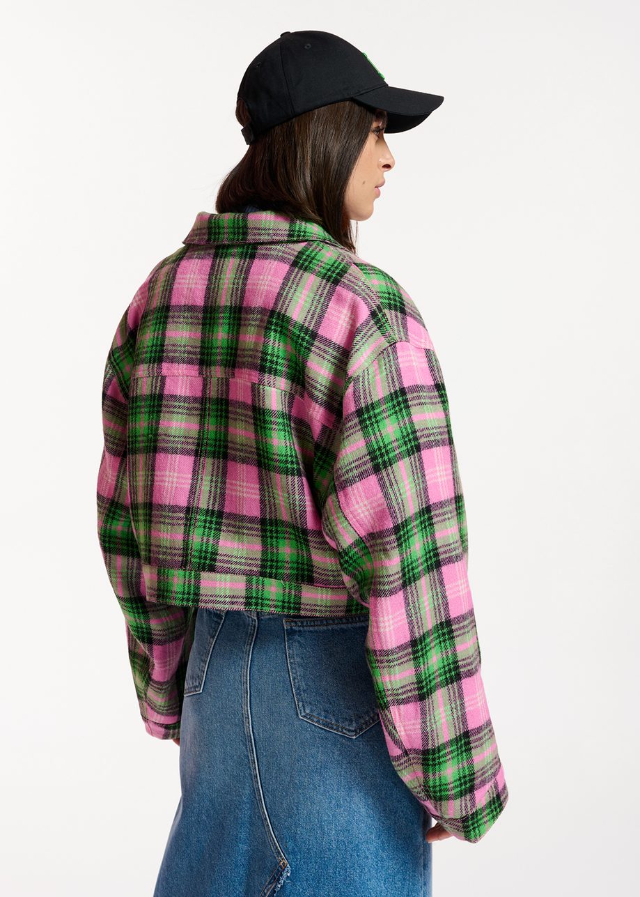 person wearing a black basball cap styles a cropped checked jacket in pink, green and black with a long maxi denim skirt, back view