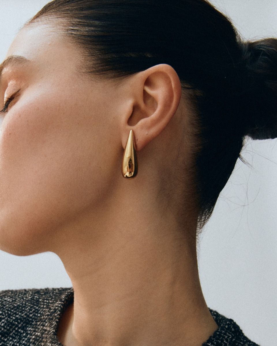 Close-up of a person with their hair in a bun, wearing the Crest Studs by EDBLAD featuring 14K gold plating, and looking to the side.