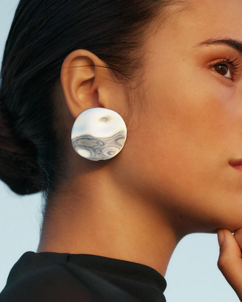 Profile view of a person wearing the bold EDBLAD Flowy Studs Maxi jewelry with a marbled design, hair tied back, and dressed in a black top.