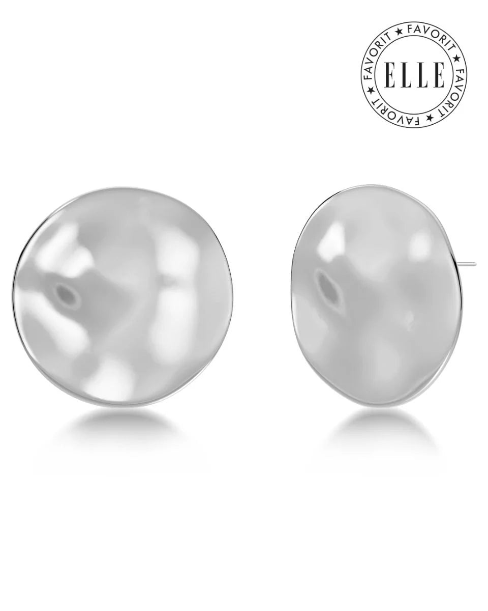 A pair of EDBLAD Flowy Studs Maxi, silver-colored round stud earrings with a reflective, slightly uneven surface. The top right corner features a circular "Elle Favorite" logo, making these bold metal jewelry pieces perfect for any occasion.