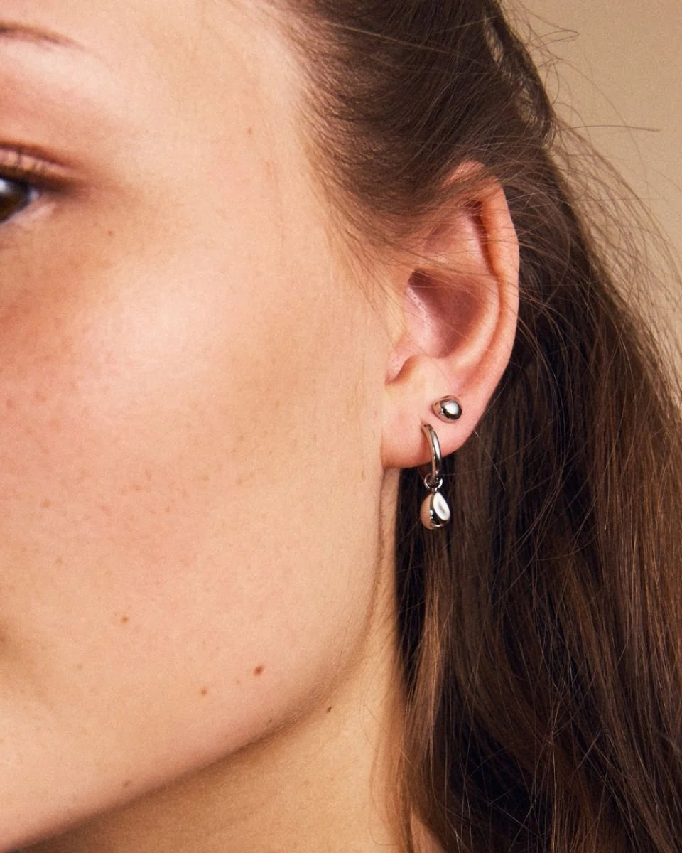 Close-up of a woman's ear adorned with two EDBLAD Lulu studs in silver, one featuring a small teardrop-shaped charm, ideal for everyday wear.