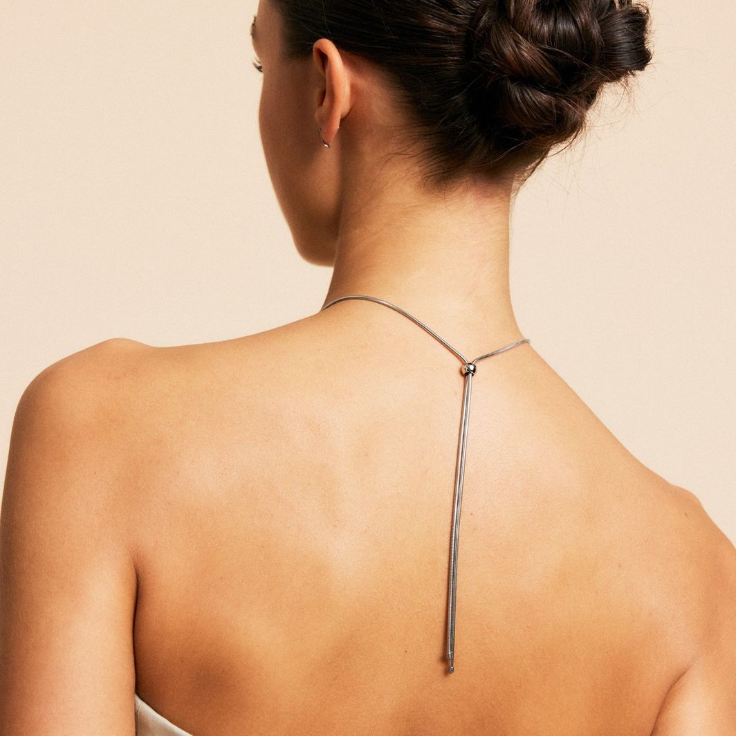 A person with light skin is shown from behind wearing a strapless top and the Melrose Necklace L by EDBLAD, featuring 14K gold plating in a geometric design. Their hair is styled in an updo.