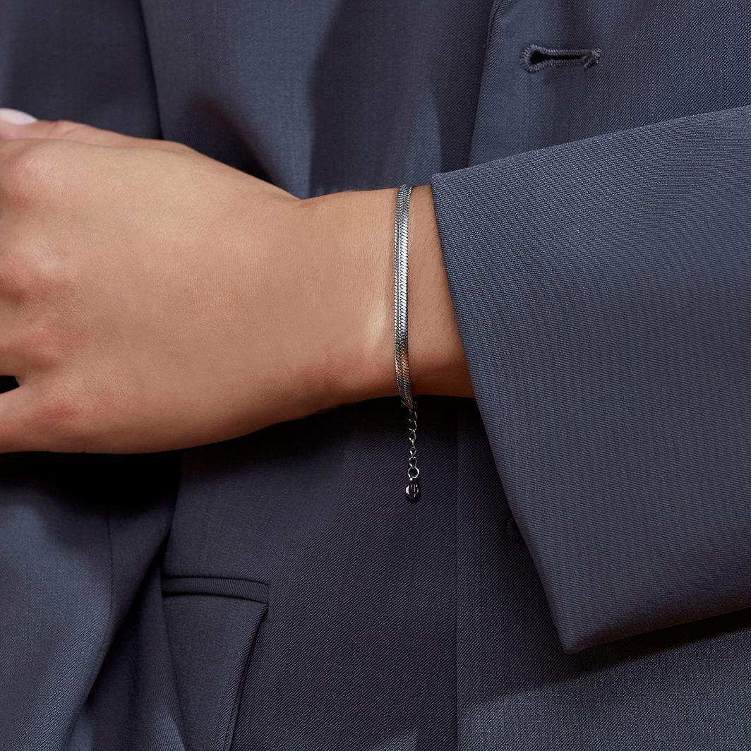 A person wearing a dark suit with an elegant, adjustable EDBLAD Herringbone Bracelet on their wrist.